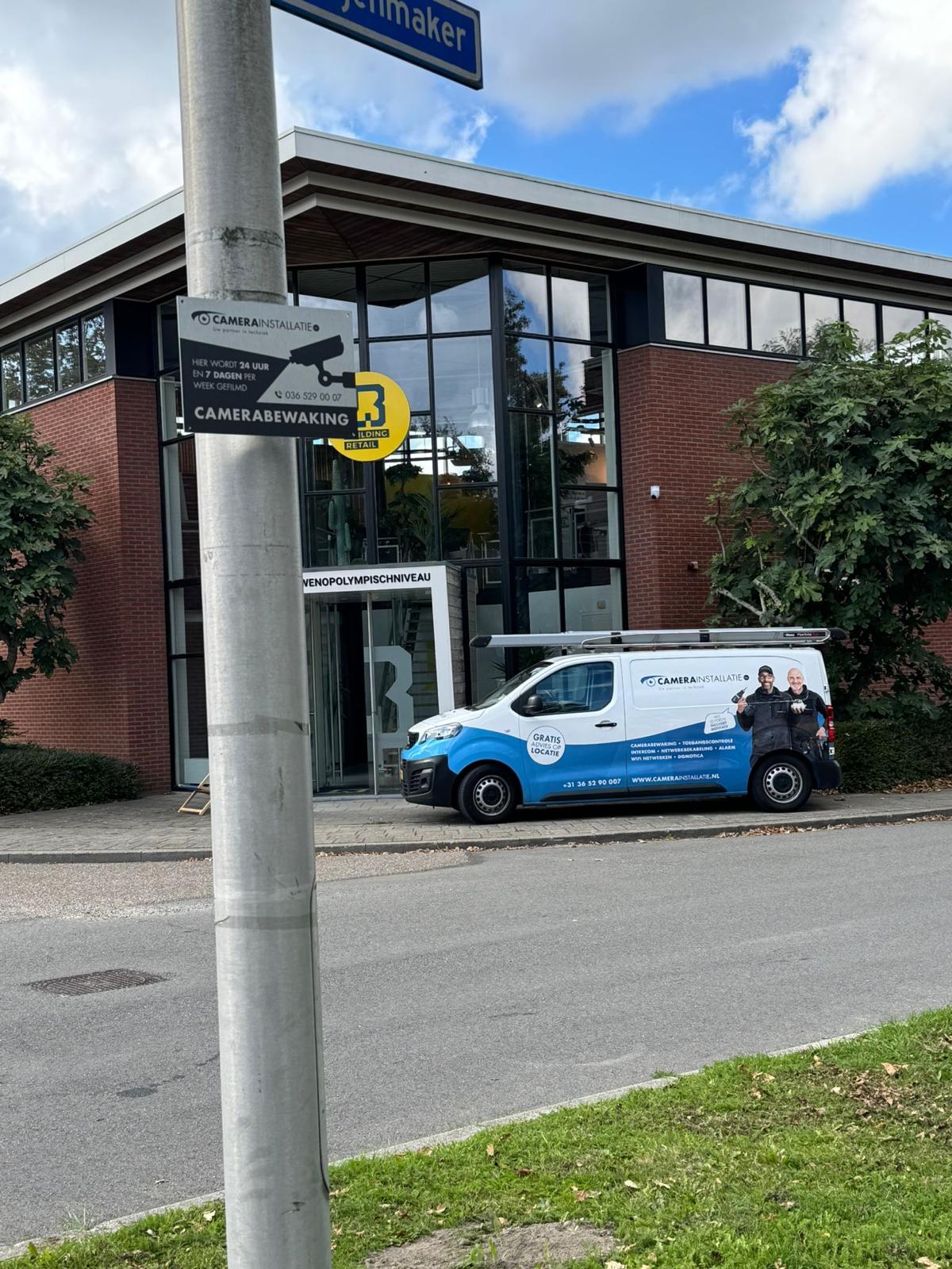Servicebus van CameraInstallatie.nl bij een bedrijfspand met camerabewakingsbord